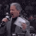 Bruce Buffer shouting into a microphone while holding a card in a suit.