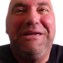 A man with a bald head and stubble has a wide, mischievous grin on his face.