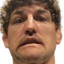A man with curly hair looks directly into the camera with wide, shocked eyes and a strained, tight-lipped grimace.