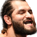 A man with a dark beard and hair makes a tense, grimacing facial expression.
