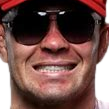 Man wearing sunglasses and a red hat showing a tense, forced grin.
