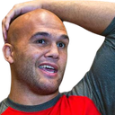 A bald man with a hand behind his head looking confused and speaking.
