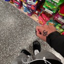 A hand with a small tattoo is held in front of a store aisle filled with colorful products.