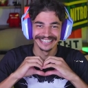 A man with a mustache wearing purple headphones smiles while forming a heart shape with his hands.