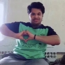 A man wearing a green shirt making a heart shape with his hands.