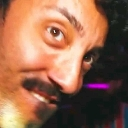 A man with a mustache looks sideways at the camera with a smirk and raised eyebrows.
