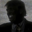 A man in deep shadow flashes a wide, bright grin while wearing a visible cross necklace.