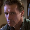 Arnold Schwarzenegger looking directly at the camera with a suspicious and intense facial expression.