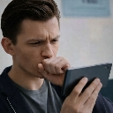 Tom Holland looking at a smartphone with a concerned expression while covering his mouth with his hand.