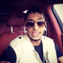 Man wearing sunglasses and a vest in a car with red seats.