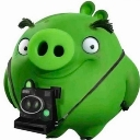 A green pig character holding a black camera and smiling mischievously.