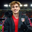 Antoine Griezmann smiling and giving a thumbs up while wearing a black jacket over a red shirt.