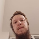 Man with a beard looking down at the camera with a suspicious and serious expression.