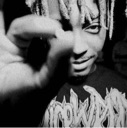 A man with dreadlocks looking intensely at the camera with his hand partially covering his face in a black and white photogr…