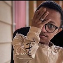 Person covering one eye with their hand while wearing glasses and looking at the camera.
