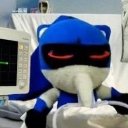 A blue plush toy lying in a hospital bed with a heart monitor screen visible in the foreground.