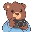 A cute brown bear in a blue shirt holding a camera and smiling.
