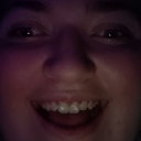 Person with a wide, mischievous grin captured in a dark, extreme close-up.