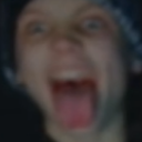 A person's face close-up, blurred and distorted while screaming with their mouth wide open.