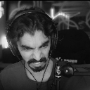 A man with a mustache and headphones grimacing with his teeth clenched in frustration.