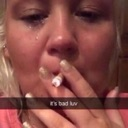 A person with a tear-streaked face holds a lit cigarette while looking directly into the camera.
