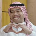 Man wearing a red and white ghutra smiling broadly while making a heart shape with his hands.