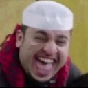 A man wearing a white kufi cap laughing with his mouth wide open.
