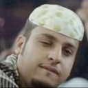 Man wearing a skullcap winks with a smug, knowing smirk on his face.