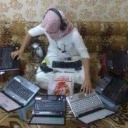 Person wearing headphones sitting on the floor surrounded by several open laptops.