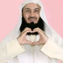 A man in traditional attire making a heart shape with his hands against a pink background.