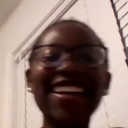 A person with glasses laughing with a wide, genuine smile in a candid, slightly blurry photo.