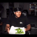 A man in a black shirt holds a plate of broccoli in the first panel, then is surrounded by a massive fire and explosion in t…