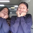 Two girls smiling shyly with their hands pressed against their cheeks.