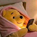 Winnie the Pooh plushie lying in bed under a pink blanket, illuminated by the light of a smartphone screen.