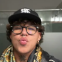 Person wearing a baseball cap and glasses puckering their lips in a kissy face expression.