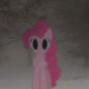 A pink pony with large, solid black eyes stands in a blurry, snowy forest.