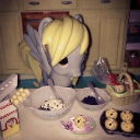 A gray pony toy stands over mixing bowls and muffins on a kitchen counter.