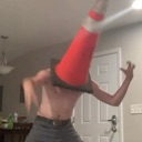 Person wearing a bright orange traffic cone on their head with arms raised in a chaotic pose.
