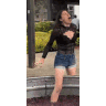 A woman in a black shirt and denim shorts loses her balance and falls while stomping grapes in a large metal vat.