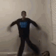 Person in a long-sleeved shirt performing a rhythmic dance move against a plain wall.