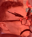 A man wearing glasses with crudely drawn angry eyebrows and a mustache, all covered in a bright red filter.