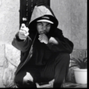 Eazy-E wearing a hoodie and cap while pointing his finger forward with a serious expression.