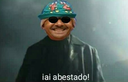 A man wearing a patterned hat and dark sunglasses smiles confidently with the text iai abestado below him.