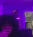 A person with curly hair stares intensely in a room bathed in deep purple light.