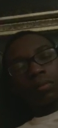 A person with glasses looking at the camera with a bored and serious expression in low lighting.