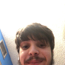 A man with dark hair and facial hair looking down at the camera with a mischievous, knowing smirk.